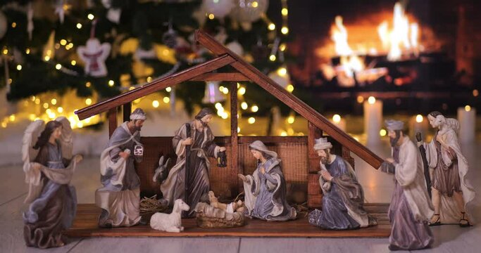 Jesus Christ Nativity scene in atmospheric lights near Christmas tree in front of fireplace. Christmas scene. Dolly shot 4k