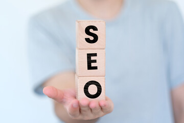 Man holding cubes vertically with SEO text on it, website concept, search engine optimization idea, wooden block cubes with SEO word, banner design - obrazy, fototapety, plakaty