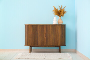 Modern chest of drawers with pampas grass near blue wall in room
