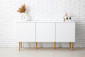 Modern chest of drawers with houseplants and pampas grass near light brick wall in room