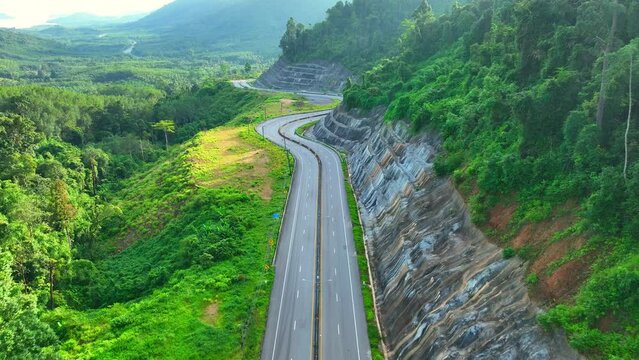 The drone flying high above, The winding road, like a ribbon of dark asphalt, meanders through the dense expanse of the rainforest, carving a remarkable path of intricate zigzags. Ranong, Thailand.

