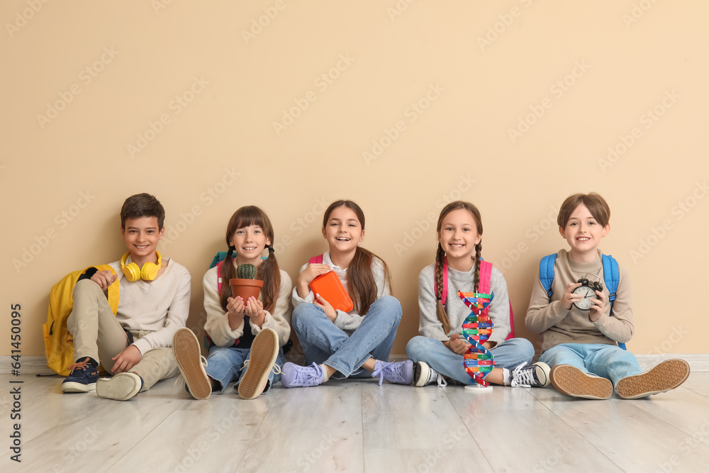 Sticker Little pupils with backpacks sitting near beige wall