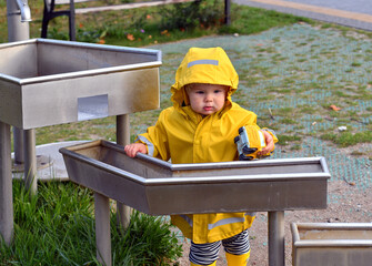 Little boy playing with water pipes in an interactive playground under the rain.