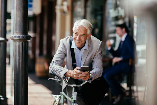Mature businessman using a smart phone while commuting to work with his bicycle