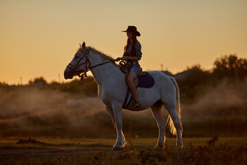 Horseback woman riding on galloping horse with red rising sun on horizon. Beautiful sunset header...