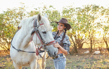 Beautiful brunette woman with long hair and horse. Portrait of a girl with cowboy hat and her horse. Beautiful girl interacting and having fun with a horse