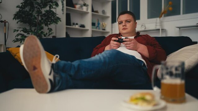 Young man playing video game and drinking beer at home, weekend activities