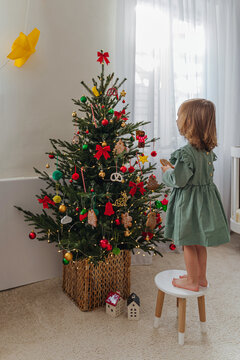 Cute little child girl is decorating the Christmas tree indoors. Merry Christmas and Happy Holidays! Christmas eve. Holiday Activity for Kids.