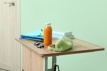 Modern school desk with backpack, bottle of juice and stationery in room near green wall