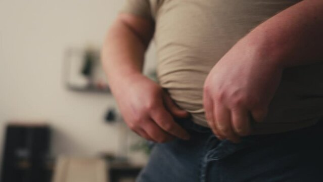 Closeup of man unable to button his jeans, overeating consequences, weight gain