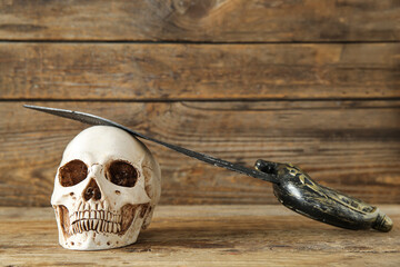 Human skull with sword on brown wooden background