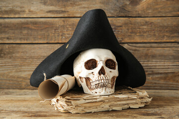 Human skull with pirate hat, scroll and old manuscripts on brown wooden background