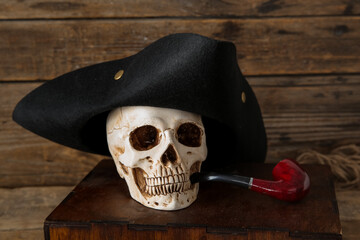 Chest with human skull, pirate hat and smoking pipe on brown wooden background