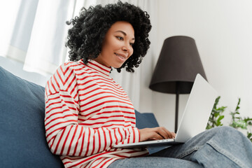 Beautiful smiling African American woman, freelancer using laptop computer working online from...
