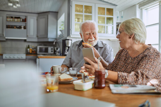 Senior couple using a smartphone and having breakfast in the morning in the kitchen