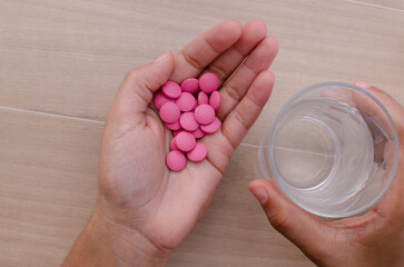Hand holding pink medicine to be taken with water. Concept of medicine and medical indication of health care for a long life.