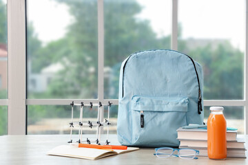 Blue school backpack with stationery, molecular model and bottle of juice on wooden table near...