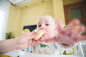 woman feeding banana to her baby who is sitting in her chair. healthy eating concept