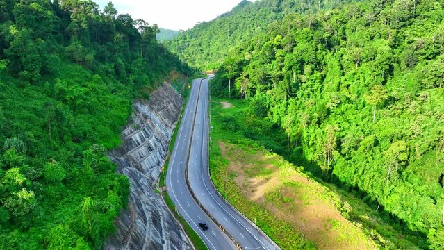 Experience the allure of Ranong Province, Thailand, as the drone unveils a captivating journey through a lush tropical rainforest, following a winding road that reveals nature's enchanting wonderland.