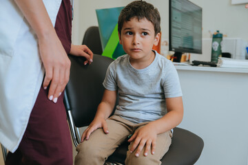 Sad frightened little boy sitting at medical office on chair looks aside with scared face...
