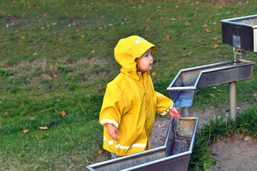 Little boy playing with water pipes in an interactive playground under the rain.