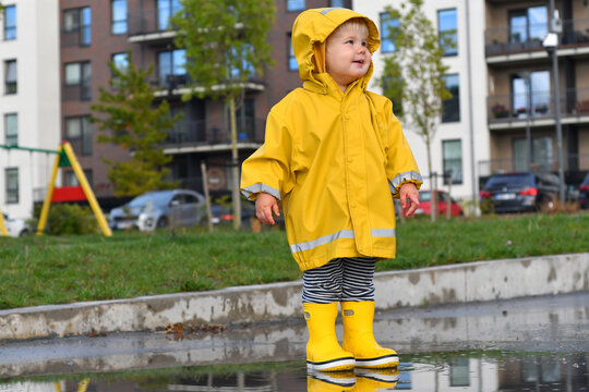 Portrait of a little child wearing yellow rain coat and wellies on a rainy day