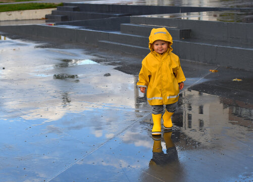Little toddler boy running through puddles on a rainy day