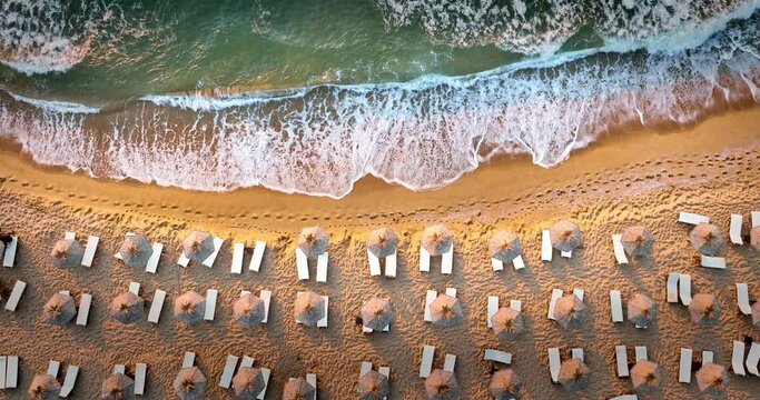 Sea sunrise over splashing waves and sandy beach shore with sun chairs and umbrellas 4K video
