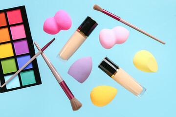 Different makeup sponges, brushes and cosmetics flying on color background