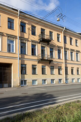 Fototapeta premium Facade of an old house in St. Petersburg. Windows, balconies, bicycle on one balcony. Sshadow of the tree on the road.
