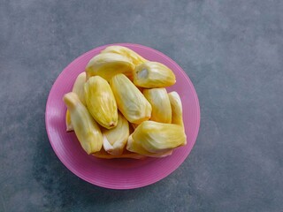 Fresh ripe jackfruit fruit on pink plate over gray background. Yellow sweet fruit. tropical fruit. yellow jackfruit on a plate