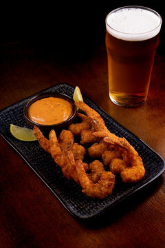 tapas portion of breaded prawns with sauce and lemon slices and chilled pint of lager beer on wooden table