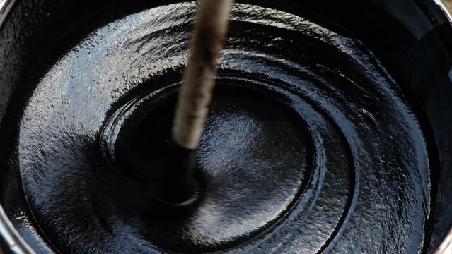 Black bitumen mastic oily liquid is stirred in a bucket (capacity) before waterproofing
