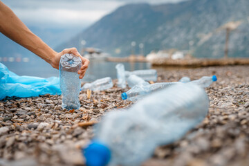 Photo of unrecognizable human hand while picking up plastic on beach.
