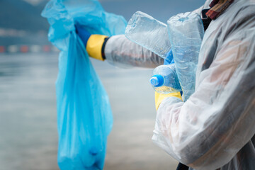 Fototapeta premium Photo of unknown person while holding garbage bag and plastic bottles in arms.
