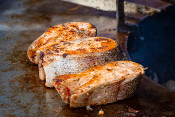 Three salmon steaks are fried on an outdoor grill, close-up. Trout steaks in herbs are fried on an outdoor grill. Street food