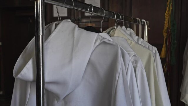 White priest's tunics hanging. Benedictine albs in cotton arranged in a row inside a sacristy. Dresses for sacred ceremony, worship and Catholic doctrine. Monastic life, preparations for mass.