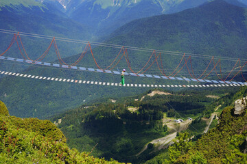 woman rouring walking on rope suspension bridge in caucasus mountains, Russia, Rosa Khutor resort