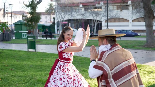 portrait couple dressed in traditional huaso clothes clapping to the rhythm of the cueca at the city square 