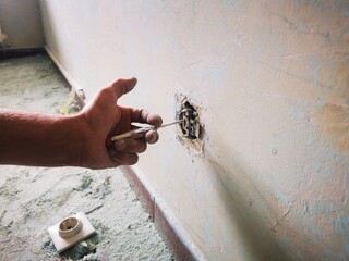 An electrician works unsafely on switches and outlets in a residential electrical system