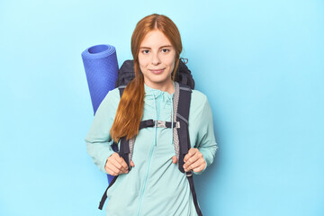 Mountaineer redhead with backpack and mat on blue background