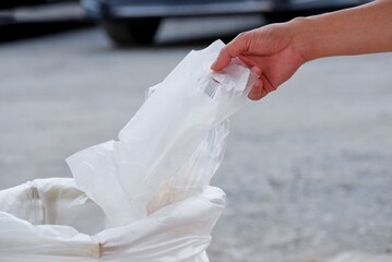 A male hand throwing a plastic bag into a recycled trash bin at the public place  