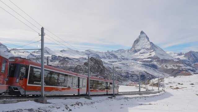 4K Static Shot of Gornergrat bahn railway climibing up the summit station with Matterhorn mountain peak background in Zermatt on a sunny winter day. Swiss Alps, Switzerland travel journey trip.
