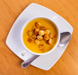 Puree soup of carrot and croutons cut into cubes served in a plate with necessary table laying