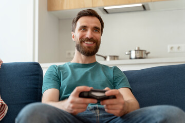 Portrait of positive bearded man on comfortable couch in apartment playing video games
