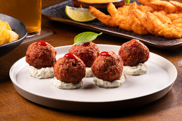 closeup on chili meatballs appetizers and plate of breaded prawns blurred in the background happy hour at the beer pub