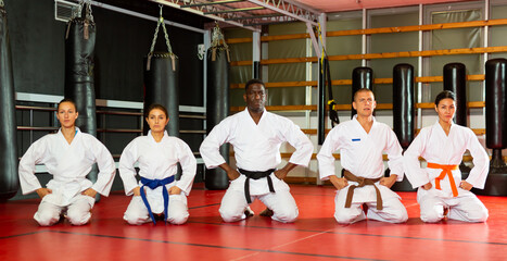 Group of multiracial people in kimono kneeling on floor during karate training.