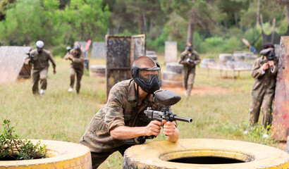 Male paintball player in protective mask standing with gun on paintball field