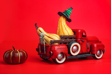Orange pumpkins in red toy truck with human skeleton on red background. Happy Halloween.