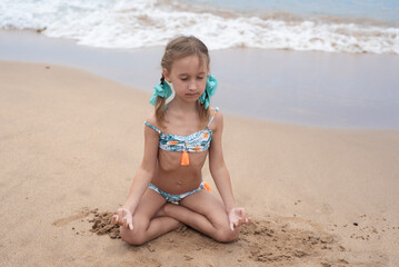 A little girl in a swimsuit runs on a sandy beach in Georgia and plays with the waves